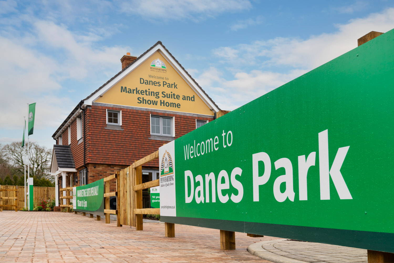 red brick house saying Danes Park Marketing Suite with wooden railings to the front displaying a green banner saying 'Danes Park'