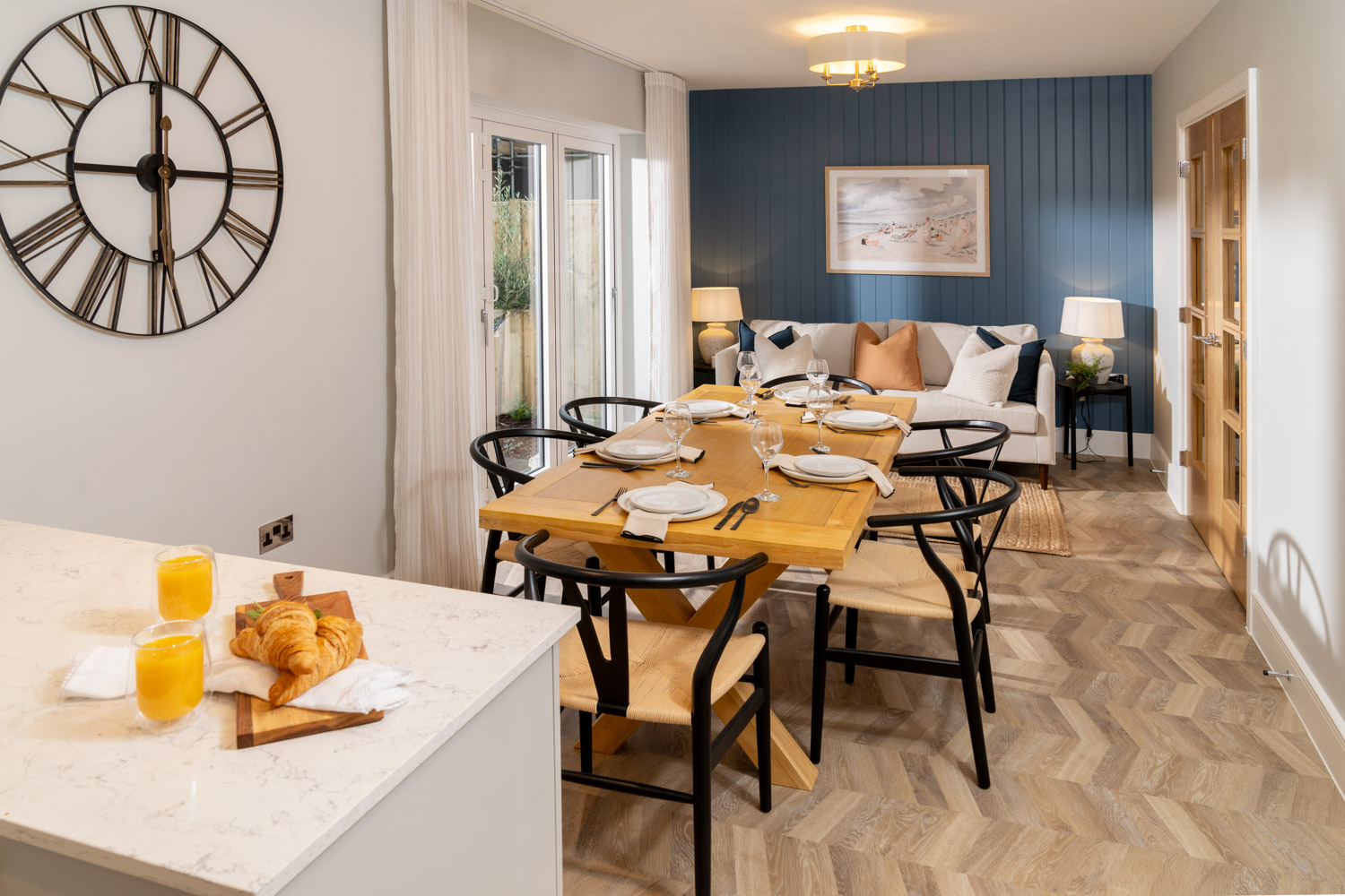 Open plan dining area with dining table and chairs at the middle with dark blue far wall and cream sofa to the rear